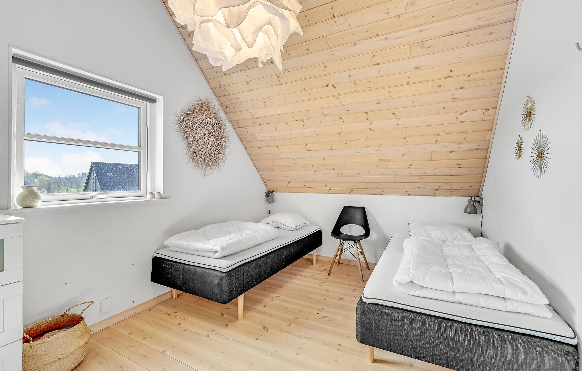 Un dormitorio con dos camas, una ventana, techo de madera y una lámpara de pared.