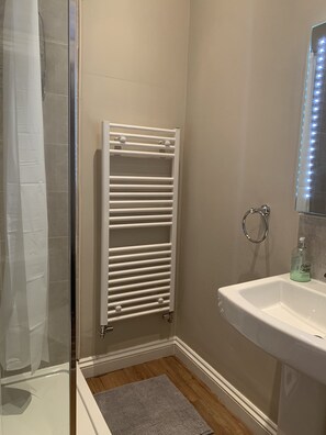 A bathroom with a white radiator, a sink with a bottle of liquid soap, and a shower area with a glass door. - Sea View Apartment in Barmouth (Barmouth)