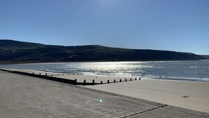 Une plage avec une promenade en béton et une vue dégagée sur l’océan et les collines qui se dressent à l’arrière-plan.