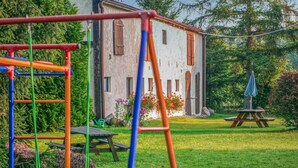Ein Spielplatz mit Schaukeln und Rutsche, einem Picknicktisch und einem Haus im Hintergrund.
