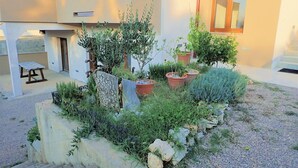 Un patio con una jardinera de piedra, plantas en macetas y un banco.