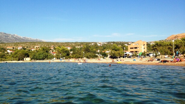 Zona costera con playa, edificios y montañas al fondo.