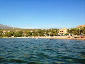 A coastal area with a beach, buildings, and mountains in the background. - Apartment Dane-50 m vom Kiestrand (Jasenice)