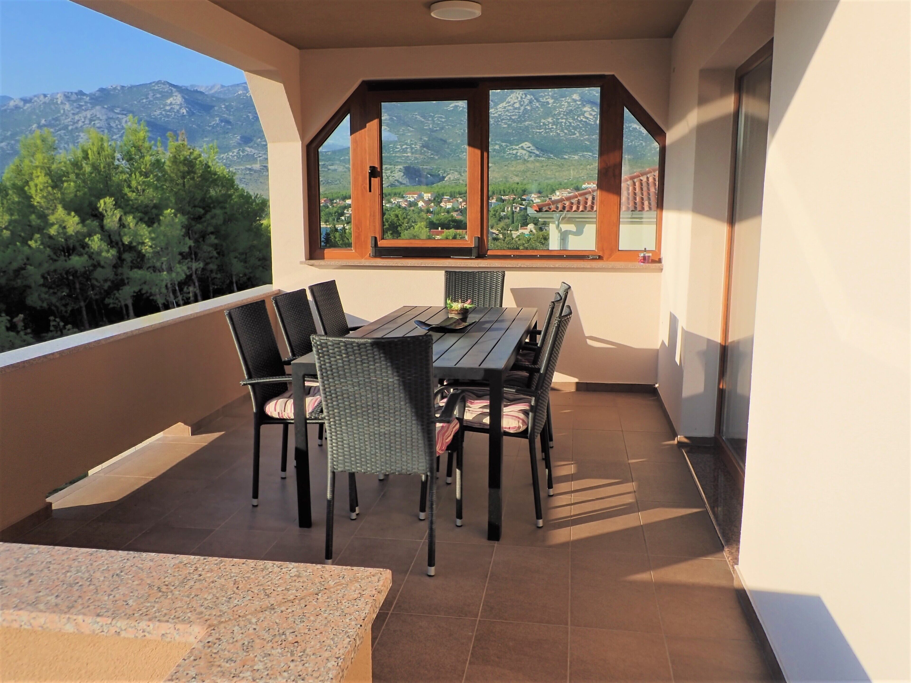 A balcony with a table and chairs, a view of mountains, and a tiled floor.