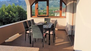 Un balcón con mesa y sillas, vistas a las montañas y suelo de baldosas.