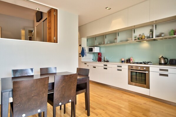 A modern kitchen with white cabinets, a microwave, a gas stove, and a dining area with a wooden table and chairs. - Lakeview @ Pounamu (Otago)