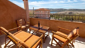 A balcony with a table and chairs, a bottle of wine, and a view of a building and landscape. - Nice home in Zubovici (Zubovici)