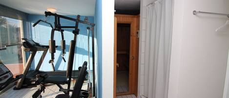 Un gimnasio con equipo de ejercicio, una ventana con persianas y una puerta de madera que da a un baño.