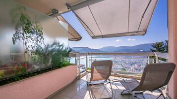 A balcony with two chairs, a glass wall with greenery, and a city view.