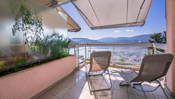 En balkon med to stole, en glasvæg med grønne planter og udsigt over byen.