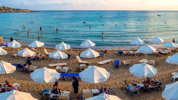 Una playa con sombrillas blancas y tumbonas, gente nadando y relajándose.