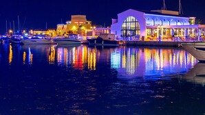 Un puerto deportivo con barcos amarrados, un edificio con amplios ventanales y una zona de restaurante muy iluminada.