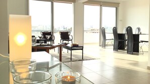 Un amplio salón con ventanas grandes, una mesa de comedor con sillas y un balcón con vistas a la ciudad.