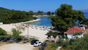 A beach with a parking area, a small building, and a view of the sea. - Hotel Vila Park Bujari Ksamil (Ksamil)