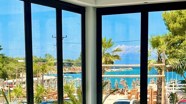 A balcony with white wicker furniture, large windows, and a view of a pool and beach area. - Hotel Vila Park Bujari Ksamil (Ksamil)