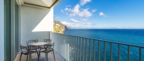 A balcony with a table and chairs overlooking a coastal view.