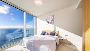 Una camera da letto con una grande finestra, un letto con copripiumino bianco e un quadro appeso al muro.