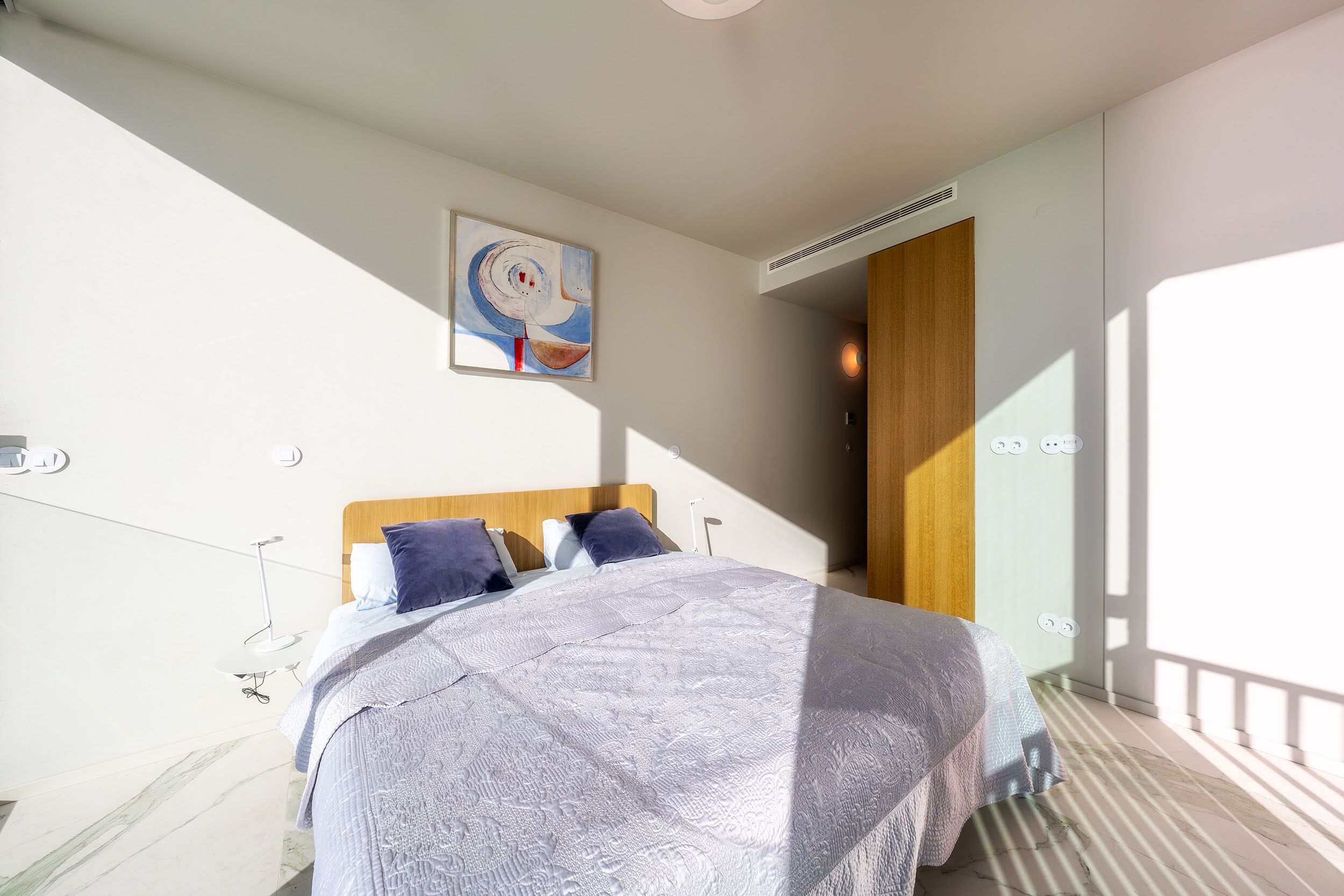 Une chambre à coucher moderne avec un grand lit, un tableau au mur et une vue sur le balcon extérieur.