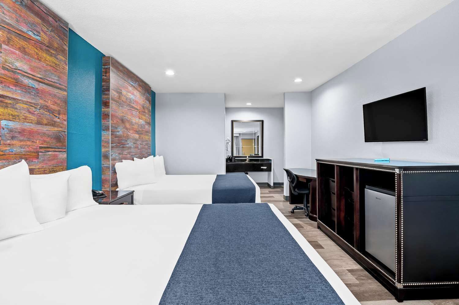 A hotel room with two beds, a desk, a television, and a large mirror.