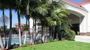 A well-maintained lawn with a swimming pool, palm trees, and a building with a red roof. - Surestay Hotel by Best Western Buena Park Anaheim (Buena Park)