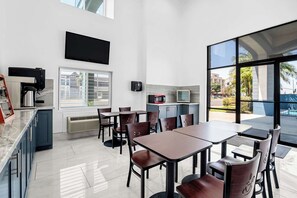Un comedor moderno con mesas y sillas, una cafetera, un televisor de pantalla plana y vistas al exterior.