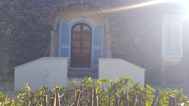 A building with a stone facade, a central arched doorway with shutters, and a small balcony. - Il Trullo del Lauro (Laureto di Fasano)