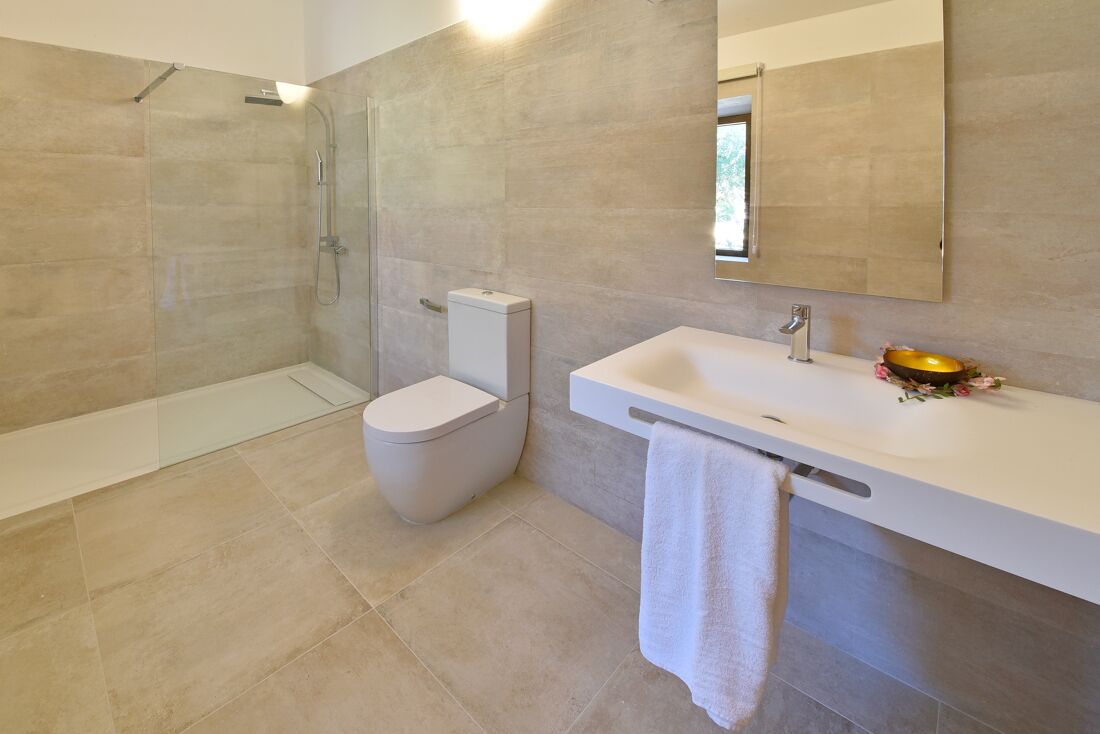 A modern bathroom with a glass-enclosed shower, a toilet, and a sink with a towel hanging on the side.