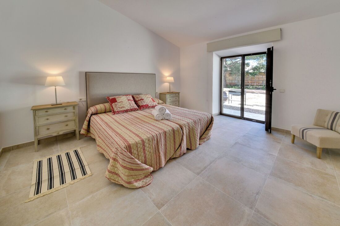 Una camera da letto con un letto, due comodini, una sedia e una porta scorrevole in vetro su un balcone.