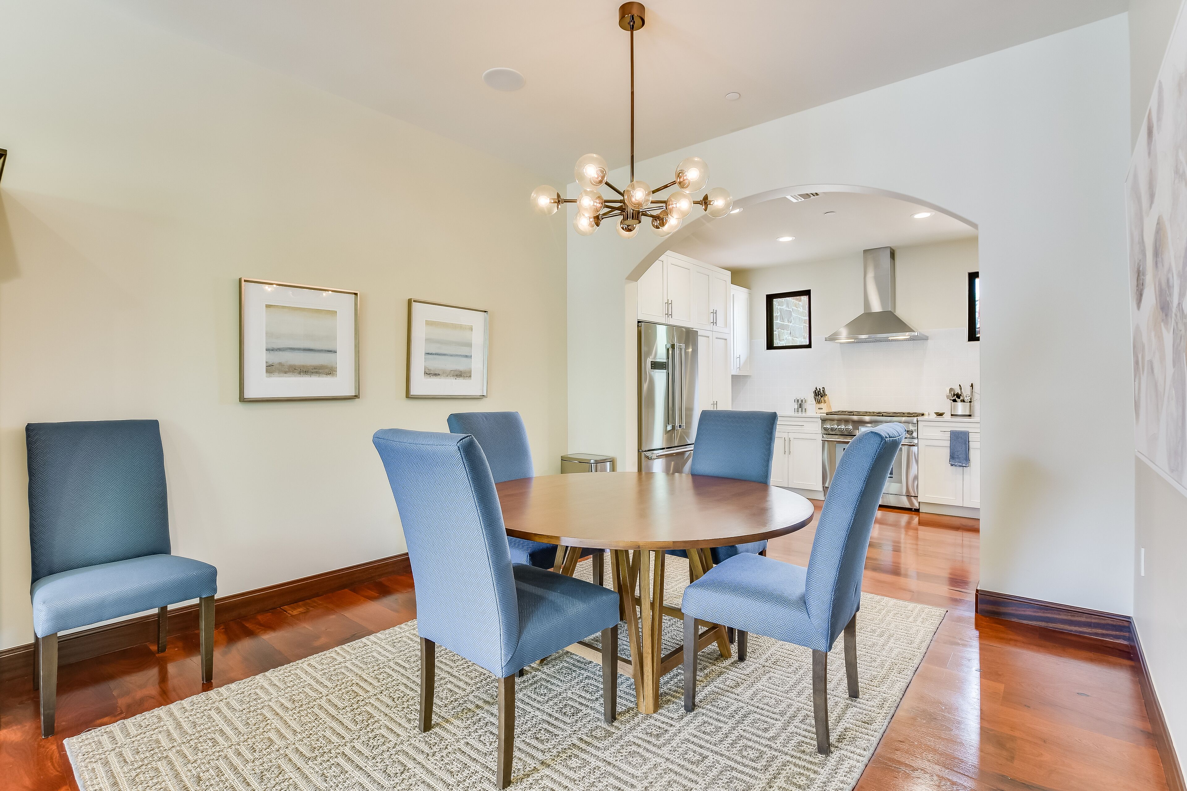 A dining area with a round table, six blue chairs, and a patterned rug.