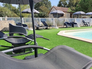 A poolside area with lounge chairs and umbrellas, surrounded by a stone wall and greenery.