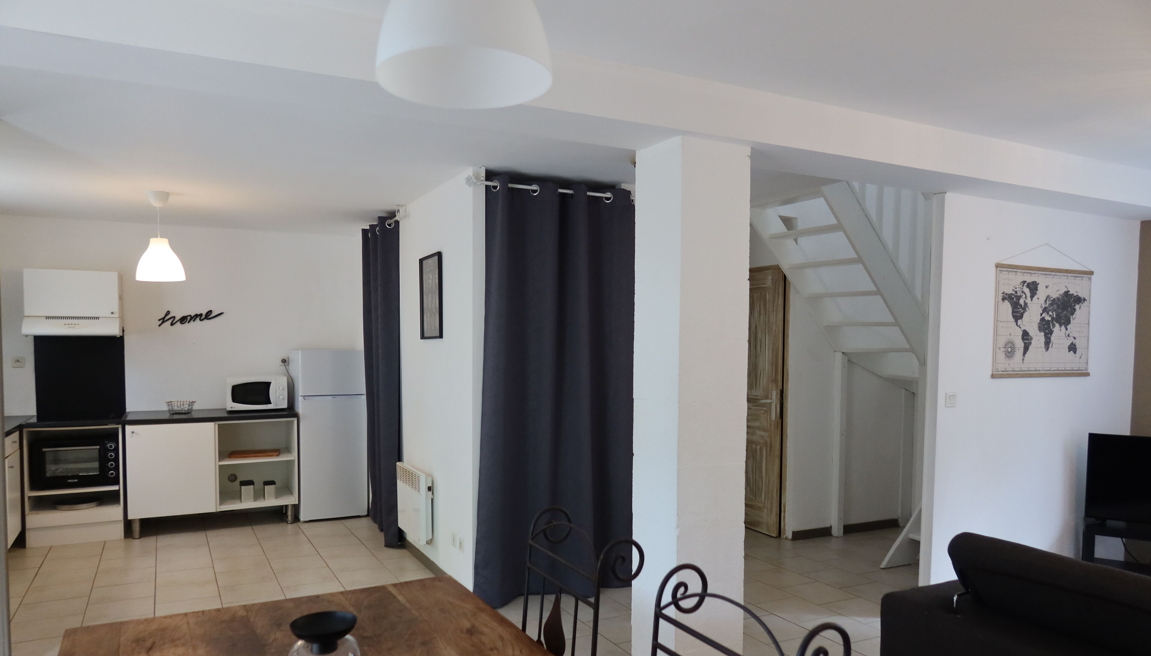 A modern kitchen with white appliances, a dining area with a brown table, and a living room with a black sofa.