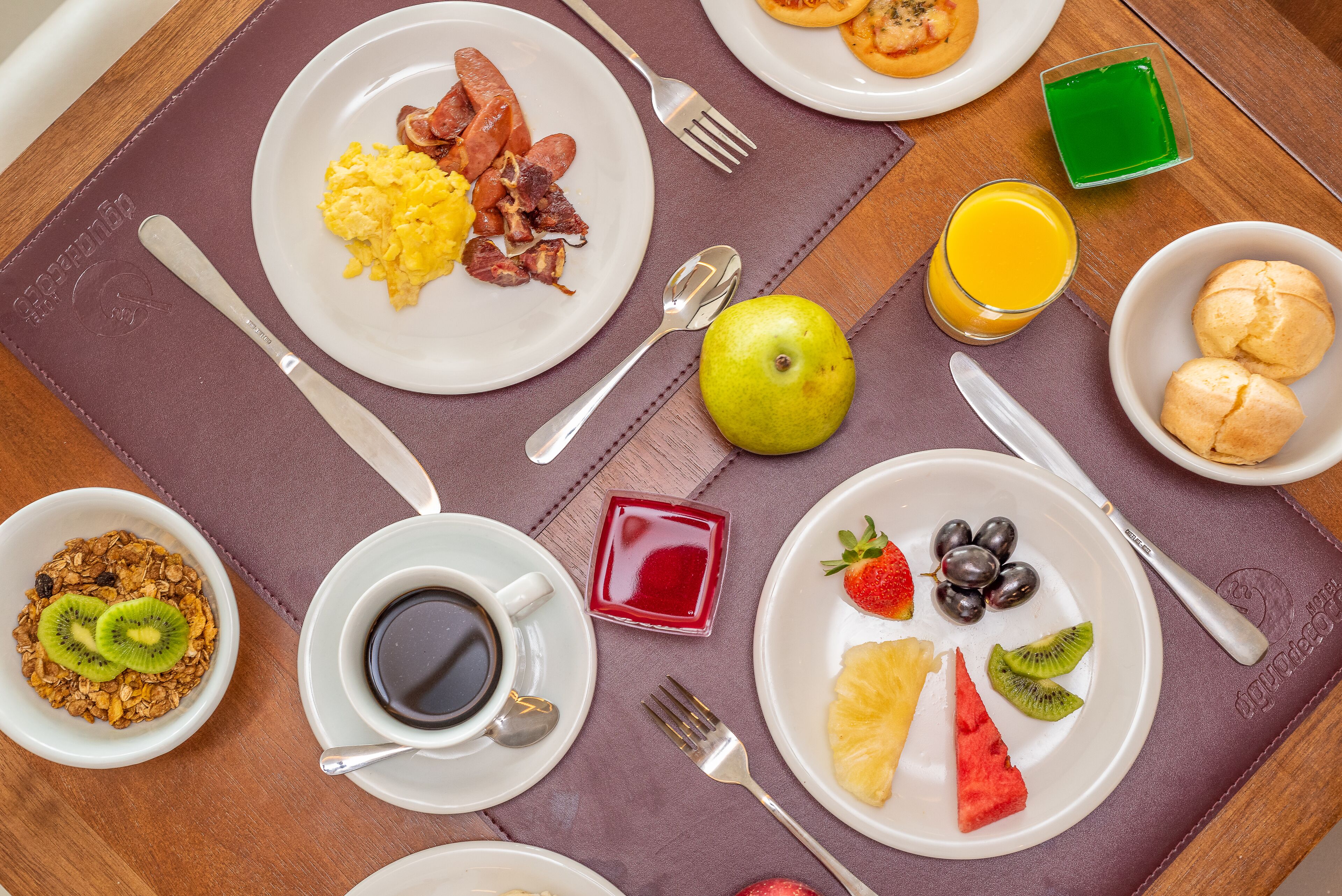 Une table dressée pour le petit-déjeuner avec des assiettes contenant des œufs, du bacon, des toasts et des fruits, ainsi qu'un verre de jus d'orange et une tasse de café.