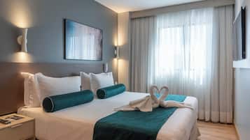 Una habitación de hotel con una cama bien hecha, una mesita de noche con lámpara, un cuadro en la pared y un amplio ventanal con cortinas.