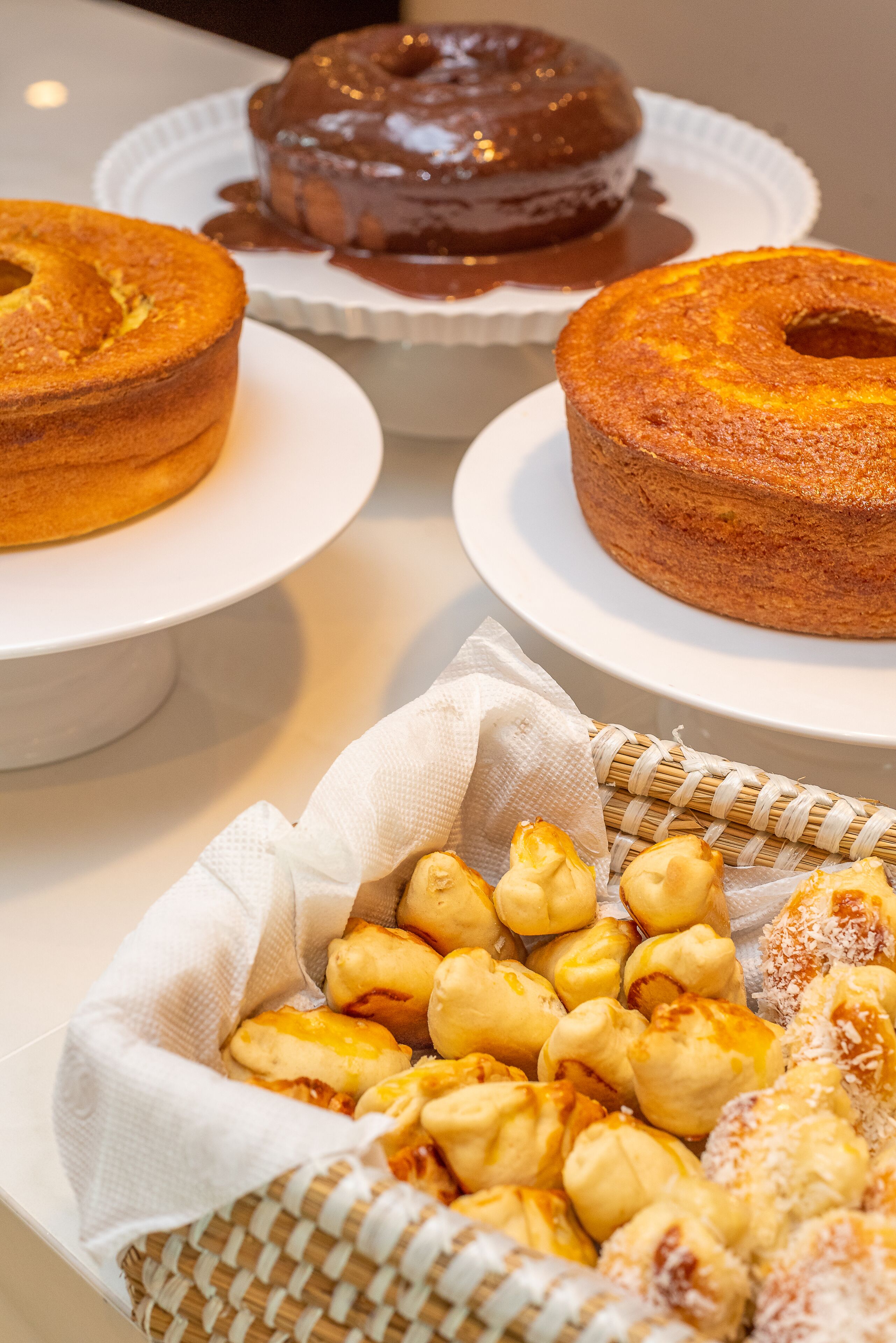 Una mesa con tres pasteles en platos blancos y una cesta de productos de repostería.