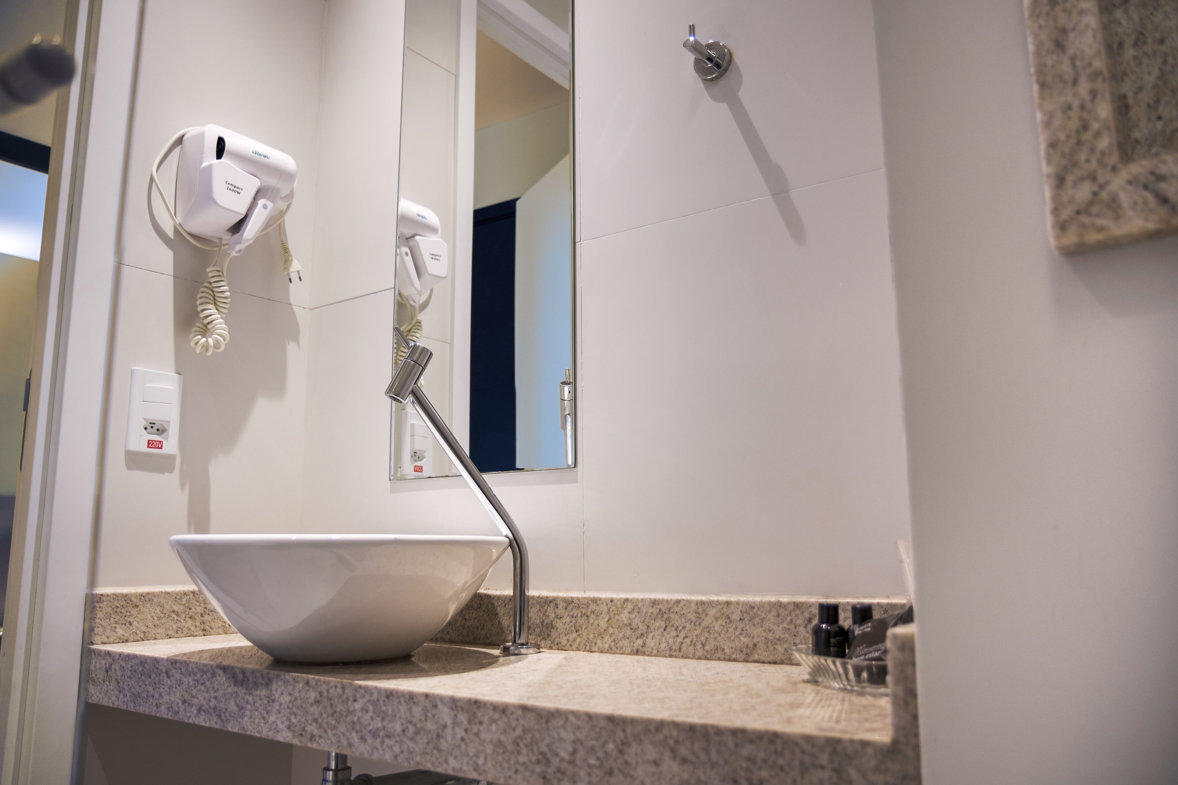 A bathroom with a white sink, a mirror, a hairdryer, and a showerhead.