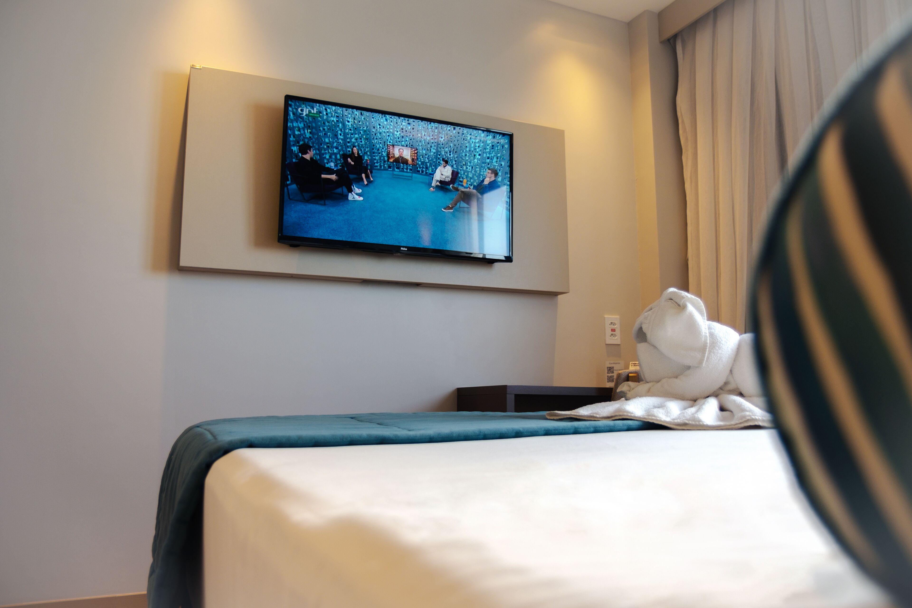 Une chambre d’hôtel avec un lit, un téléviseur à écran plat fixé au mur et une fen être avec des rideaux.