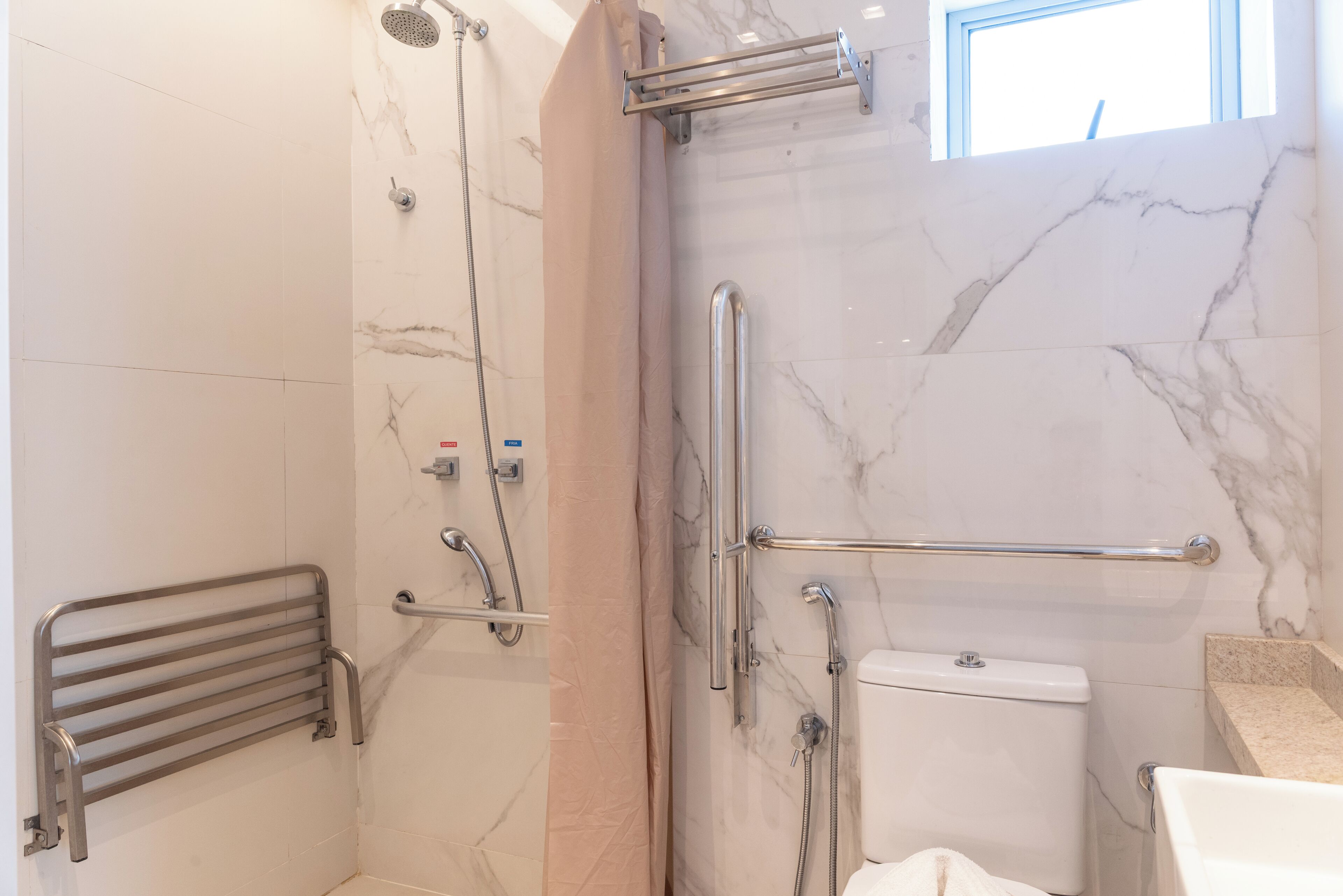 A bathroom with a shower, toilet, and handrails.