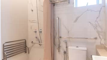 Un baño con ducha, inodoro y barras de apoyo.