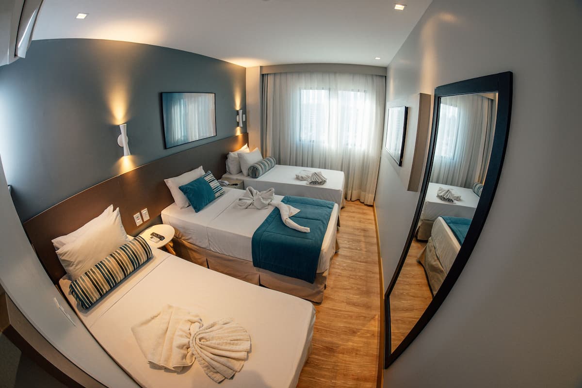 A hotel room with two beds, a large mirror, and a view of the outdoors.