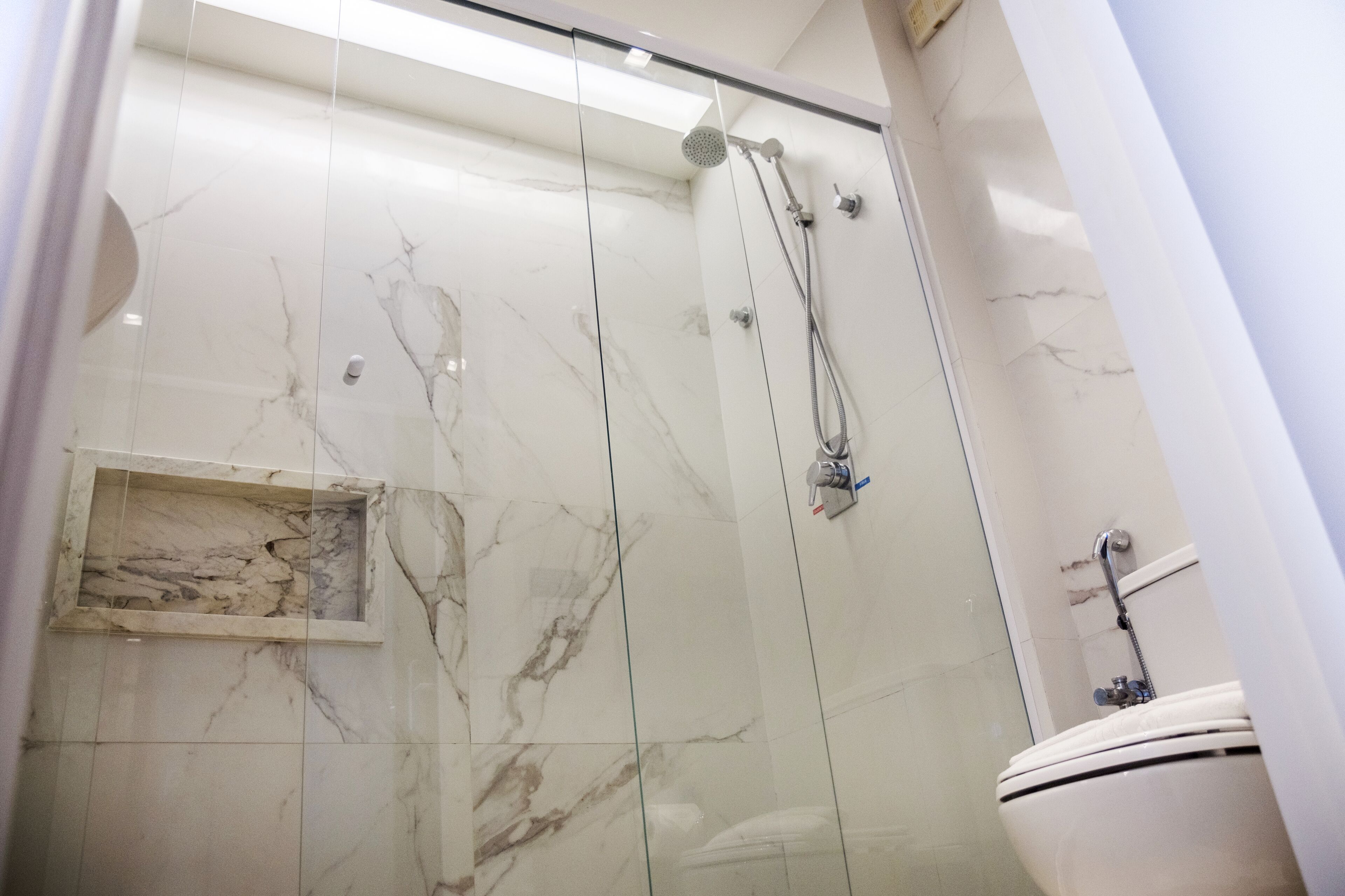 A bathroom with a glass-enclosed shower, a marble-tiled wall, and a white toilet.
