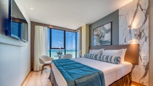 Habitación de hotel moderna con una cama grande, un escritorio con silla, vista al océano y pared de mármol.