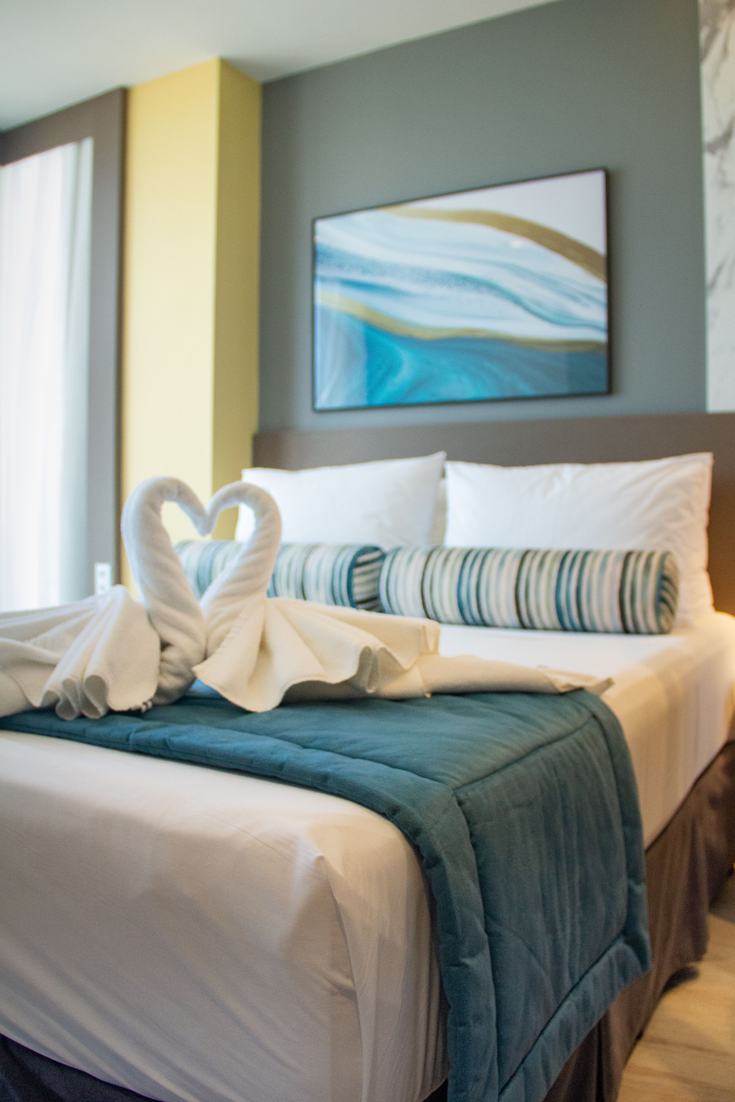 Habitación de hotel con cama, almohadas y una decoración de toallas con forma de corazón.