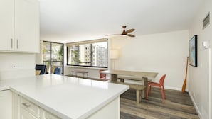 Een moderne keuken met witte kastjes, een centraal eiland en een eethoek met een houten tafel en rode stoelen.