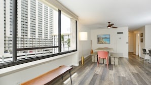 Een modern appartement met een groot raam, een houten bankje, een eethoek met tafel en stoelen, en een plafondventilator.