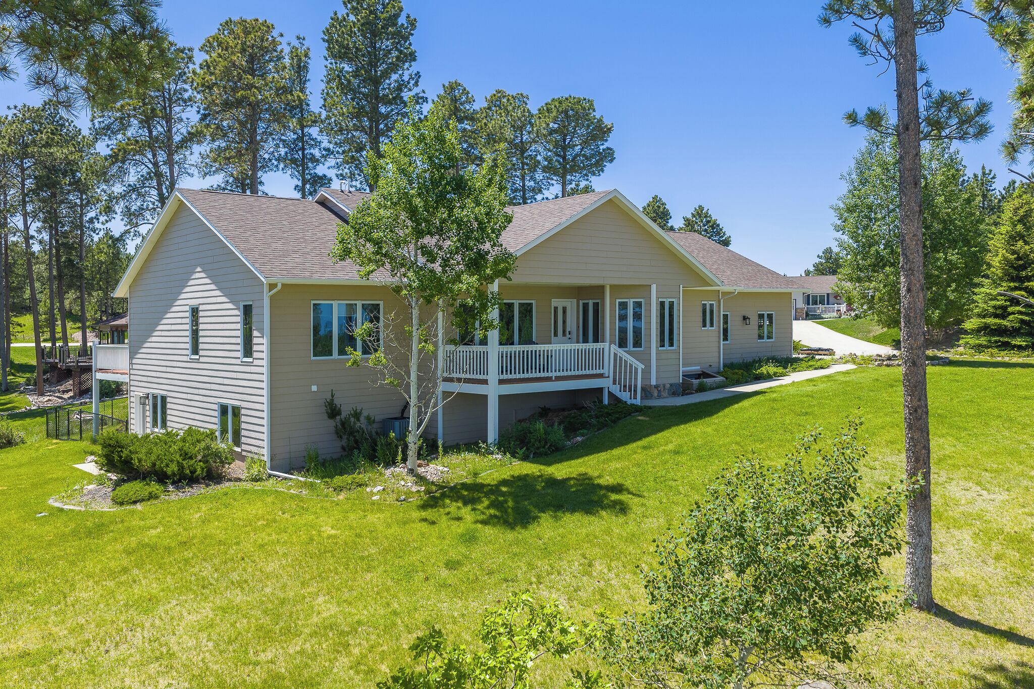 A two-story house with a front deck, surrounded by a well-maintained lawn and tall trees.