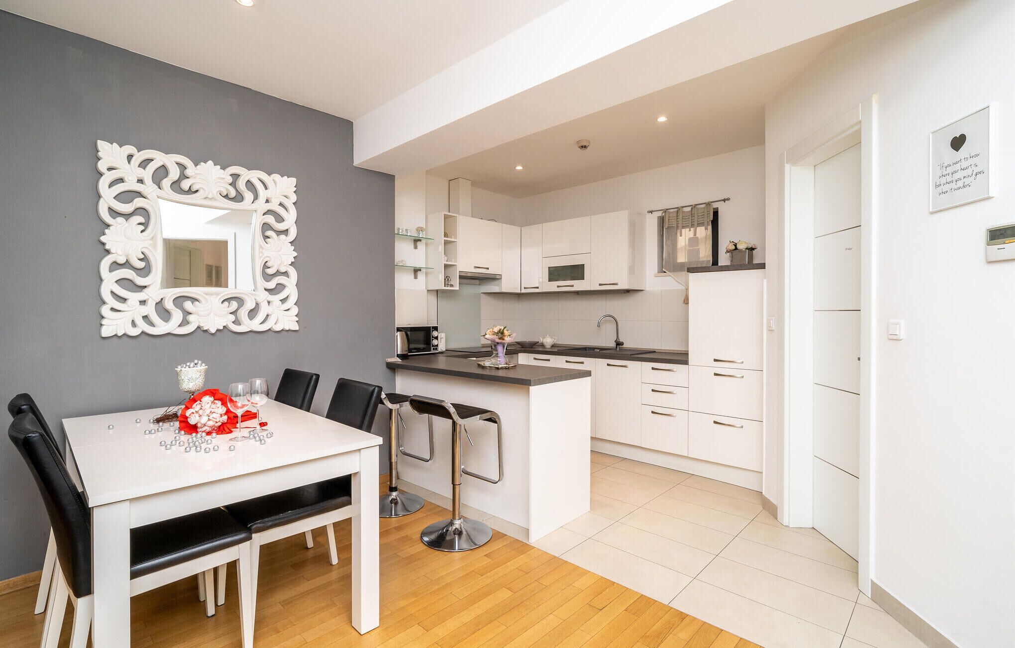 A modern kitchen with white cabinets, a central island, and a dining area with a white table and chairs.