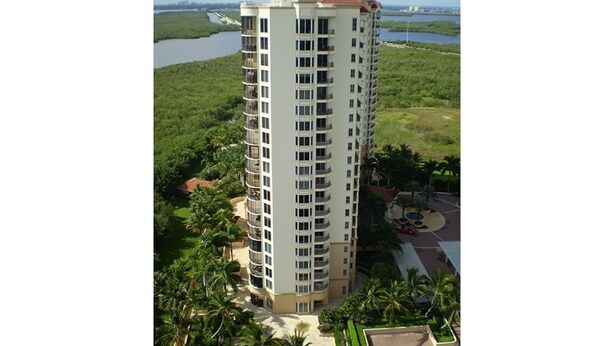 A high-rise building with multiple balconies, surrounded by greenery and a body of water. - A Slice of Heaven (Naples)
