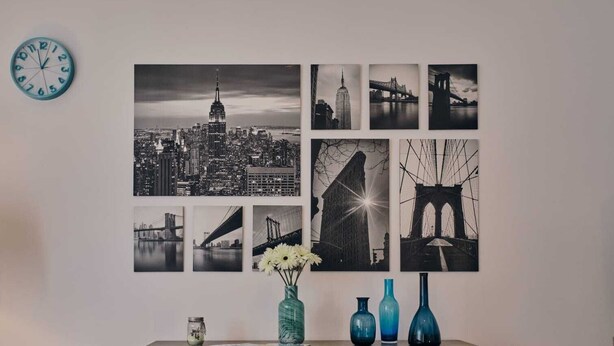 A wall with multiple black and white photographs of cityscapes and bridges, a clock, and three vases on a wooden dresser. - Casa Vacanze Asariel Splendido Appartamento Vista Mare e Centro Città (Brindisi)