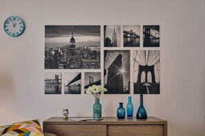A wall with multiple black and white photographs of cityscapes and bridges, a clock, and three vases on a wooden dresser.