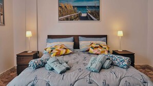 A bedroom with a bed, two nightstands, a painting of a beach scene, and a patterned bedspread. - Casa Vacanze Asariel Splendido Appartamento Vista Mare e Centro Città (Brindisi)